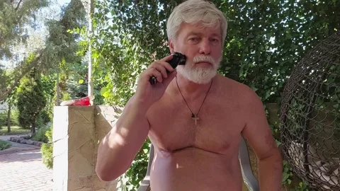 A man trims his grey beard with an electric razor Stock Footage 305338982