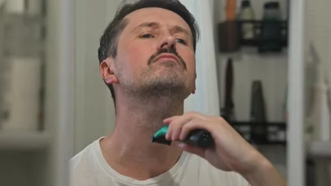 A man trims his mustache and beard with an electric trimmer in a bathroom Stock-Footage 337111552