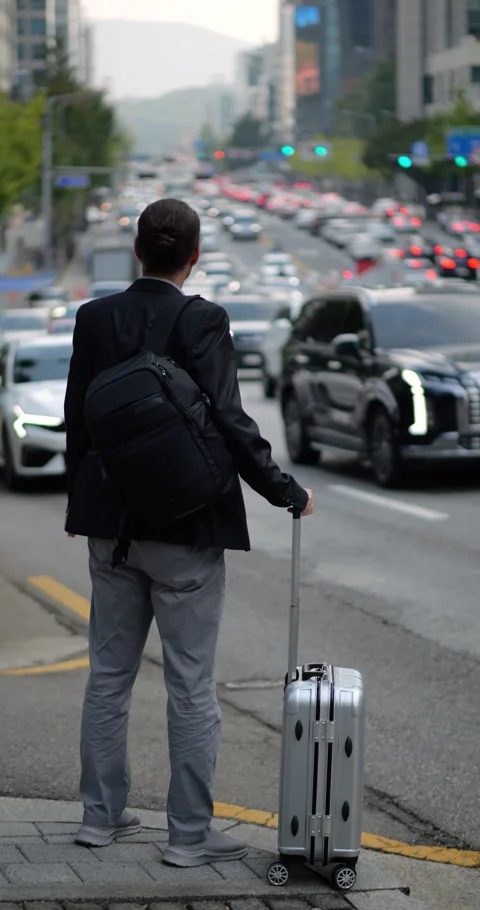 Man with trolley case wait at side of city road, blurred traffic on background Stock Footage 303989704