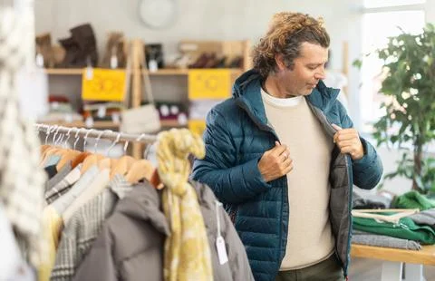 Man try on down jacket in front of mirror in clothes store Photos