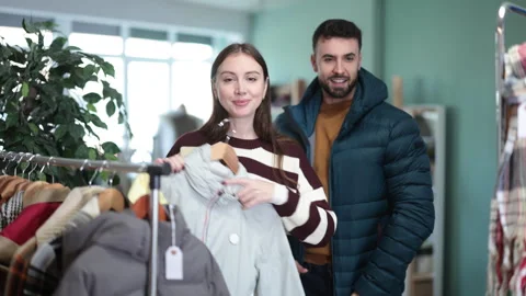 Man try on down jacket, woman elect coat or jacket. Family mutual shopping time Stock Footage 330394298