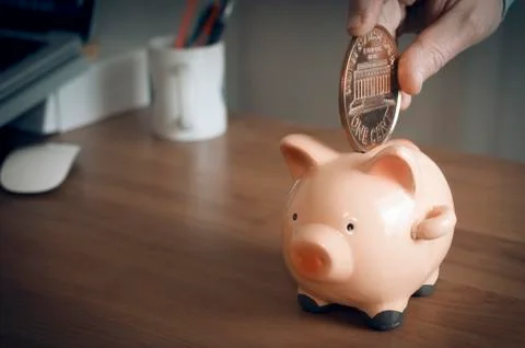 Man try to put a giant one cent coin into a small piggy bank. Stock Photos