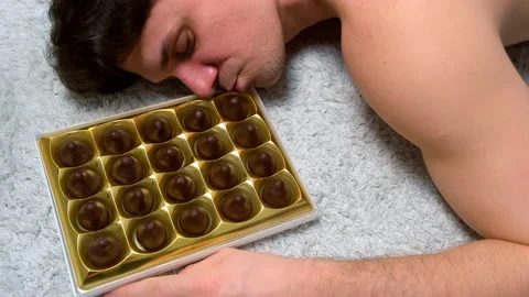 Man is trying to eat box of chocolates sweets, chocolate candy set. Video stock 238353141