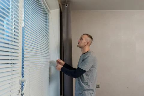 A man is trying to fix a malfunction in the window blind mechanism. Opening.. Stock Photos