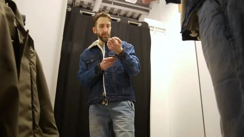A man trying on a fleece lined denim jacket in a fitting room Stock Footage 303688030