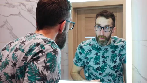 A man trying on glasses in front of a bathroom mirror Stock Footage 309294298