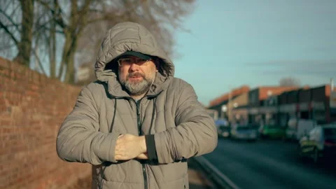 Man trying to keep warm on street in residential area with houses in city. Male Stock Footage 303153300