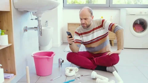Man trying to stop a water leak and calling a plumber Stock Footage 297856209