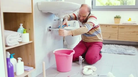 Man trying to stop a water leak and calling a plumber Stock Footage 297856216