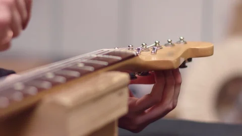 Man tunes guitar strings with peg winder Stock Footage 102056665