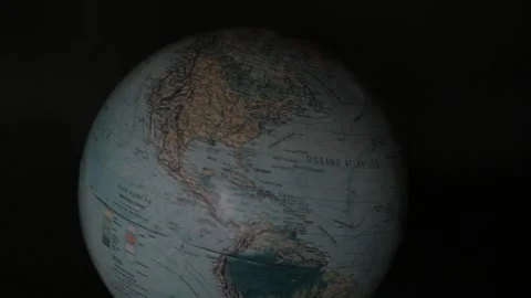 A man turning a globe in a dark background around with his hand and pointing to Stock Footage 163767483