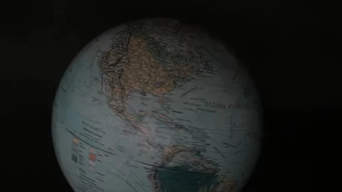 A man turning a globe in a dark background around with his hand and pointing to  Stock Footage 163773662
