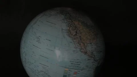 A man turning a globe in a dark background around with his hand and pointing to  Stock Footage 163773671