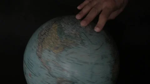A man turning a globe in a dark background around with his hand and pointing to  Vídeos de archivo 163773683