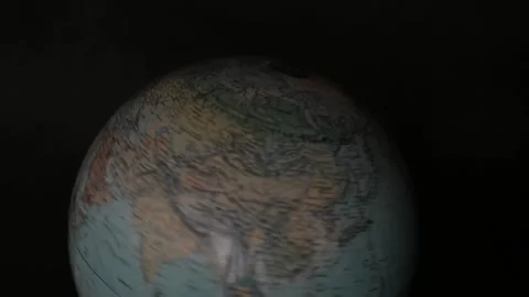 A man turning a globe in a dark background around with his hand and pointing to  Stock Footage 163773697