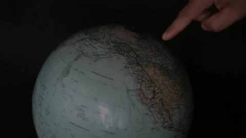 A man turning a globe in a dark background around with his hand and pointing to  Vídeos de archivo 163773705