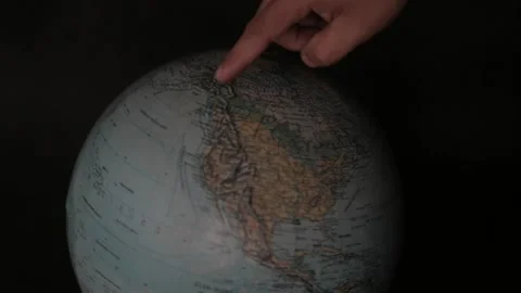A man turning a globe in a dark background around with his hand and pointing to  Stock Footage 163773730