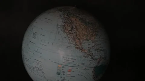 A man turning a globe in a dark background around with his hand and pointing to  Stock Footage 163773747