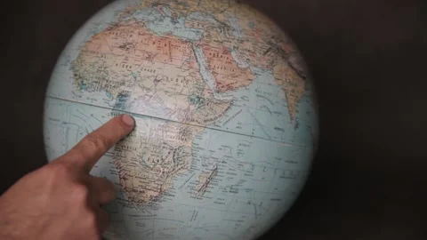 A man turning a globe in a dark background around with his hand and pointing to  Stock Footage 163773845