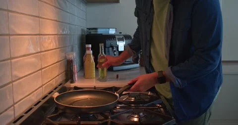Man is turning on kitchen stove, placing nonstick pan, pouring oil, grabbing Stock Footage 340611135