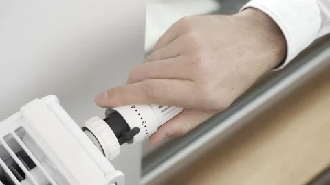 The man turns off the heating by setting the radiator thermostat to a minimum Stock Footage 211621403