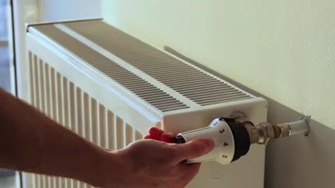 The man turns off the heating by setting the thermostat of the radiator to 库存影片 242503396