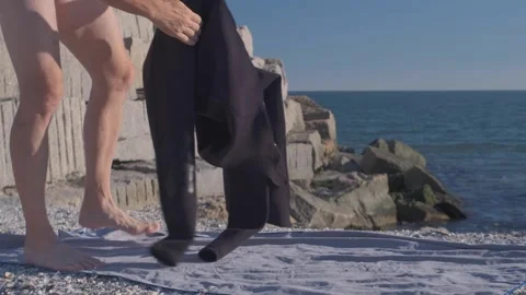 A Man Turns His Diving Suit Inside Out On The Seashore To Put It On. Stock Footage 325071034