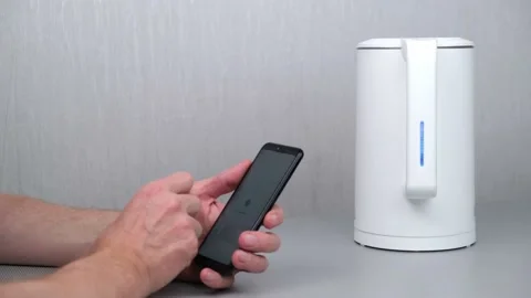 The man turns on the kettle using an application on his smartphone. Smart home. Video stock 167246063
