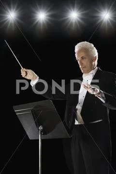 Man in tuxedo conducting under lights Stock Photos