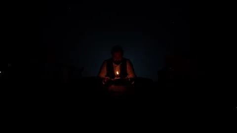 A man in the twilight sits at a table, holds a candle in his hands and looks at Stock Footage 242323475