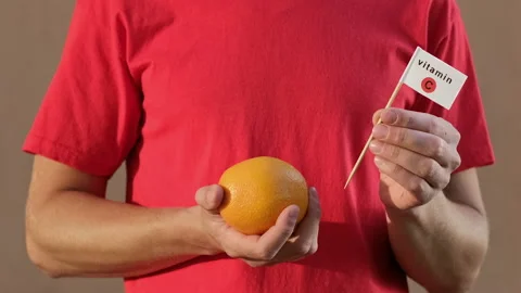 Man twirls an orange and inserts a flag with the inscription "vitamin C" Stockbeeldmateriaal 141841610