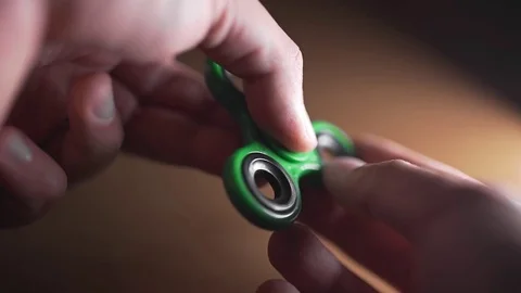 Man twists green spinner in his hand, fidget spinner is twisting round and round Stock Footage 80036778