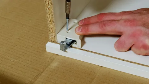 Man twists screw connecting hinges for sliding carcass put on cardboard Stock Footage 304399954