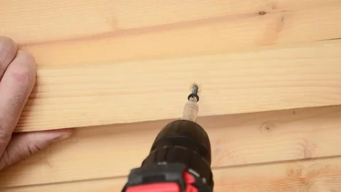 A man twists a self-tapping screw with an electric screwdriver into a wooden Video stock 237607856
