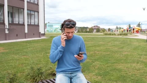 Man with two mobile phones sitting on the bench near the home. Calling of both Stock Footage 102451601