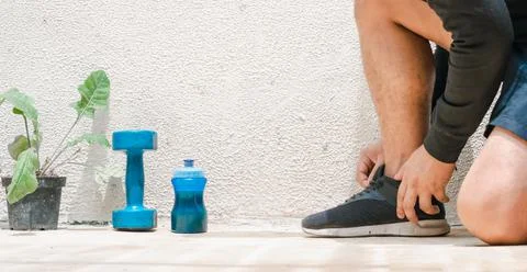 Man tying his shoes on the floor next to blue dumbbell and bottle with water, Stock Photos