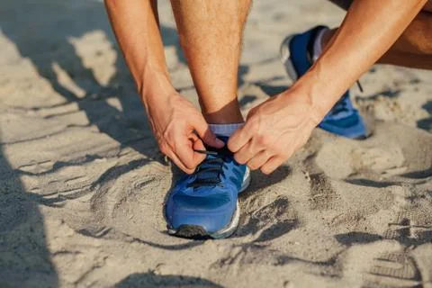 Man is tying shoelace while standing on the sand. Stock Photos