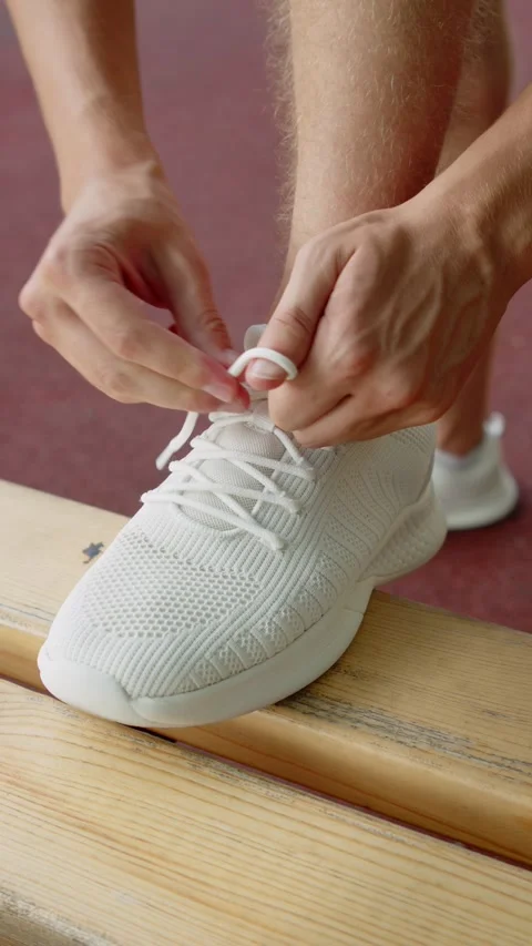 Man tying shoelaces before a workout. Tying a white sneaker on a bench clos.. Vídeos de archivo 341458139