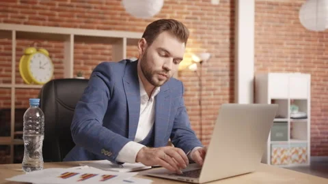 A man types on a laptop and writes in a notebook then beats water from a bottle 库存影片 190998378