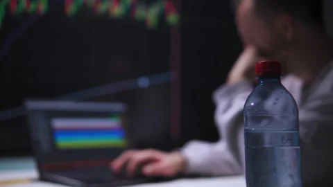 Man types on a laptop in front of a large screen with stock charts in an Stock Footage 317165319