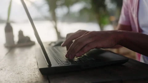 Man types on laptop at sunset beach cafe, freelance writer works remotely near Stock Footage 281243658