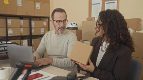 Man types on laptop while colleague holds a parcel and scans a barcode at a.. Vidéo 339237601