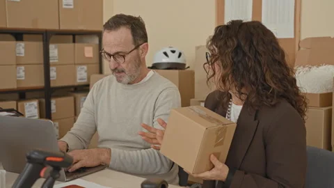 Man types on laptop while woman holds a parcel and points finger toward lab.. Stock Footage 339240966