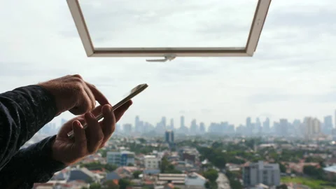 A man types a message on a smartphone against the background of an open window Stock Footage 122104703