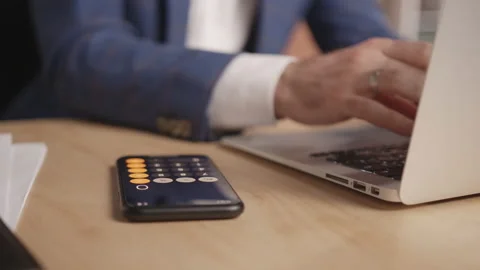 A man types something on a laptop, then counts in the calculator on the phone 库存影片 191883460