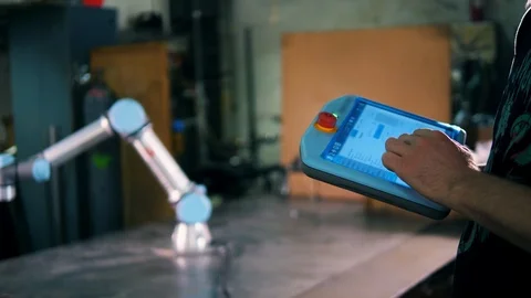 Man types on a tablet, controlling a robotic arm. Video stock 111875372