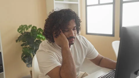 Man typing on computer with hand on face at desk in building, seated by mon.. Stock Footage 337395668