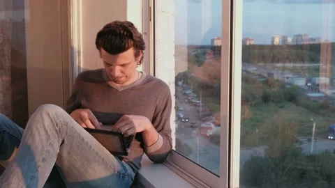 Man typing on a computer sitting on a balcony overlooking the city at sunset in Video stock 102449600