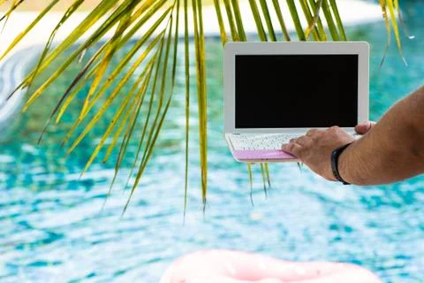 A man is typing on his laptop while sitting by the pool. Mens hands on the Stock Photos