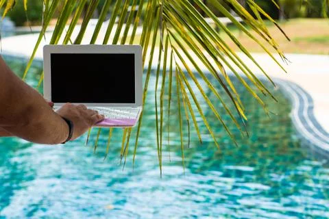A man is typing on his laptop while sitting by the pool. Mens hands on the Stock Photos